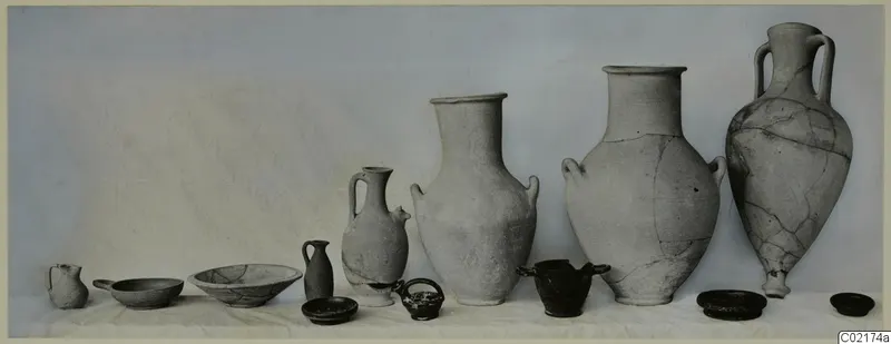 Row of pottery vessels from Marion, Tomb 45, including jugs and bowls, set out on a white cloth.