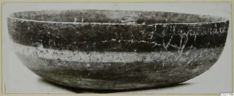 Side view of a rounded bowl with a wide open mouth, dark surface and a pale band around the body