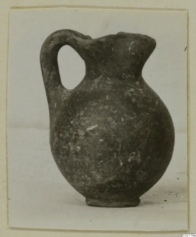 Black-on-Red jug with a single loop handle and ring base, photographed on a pale surface