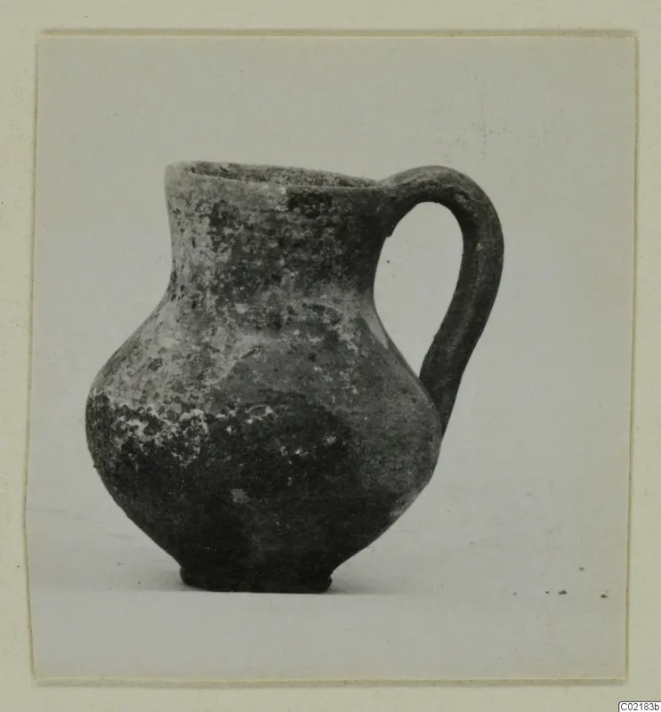 Pottery Red Slip jug with a single loop handle, photographed on a plain background