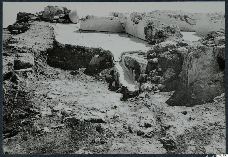Excavated ruins at the palace at Vouni, with low pale walls and a sunken area in the centre.