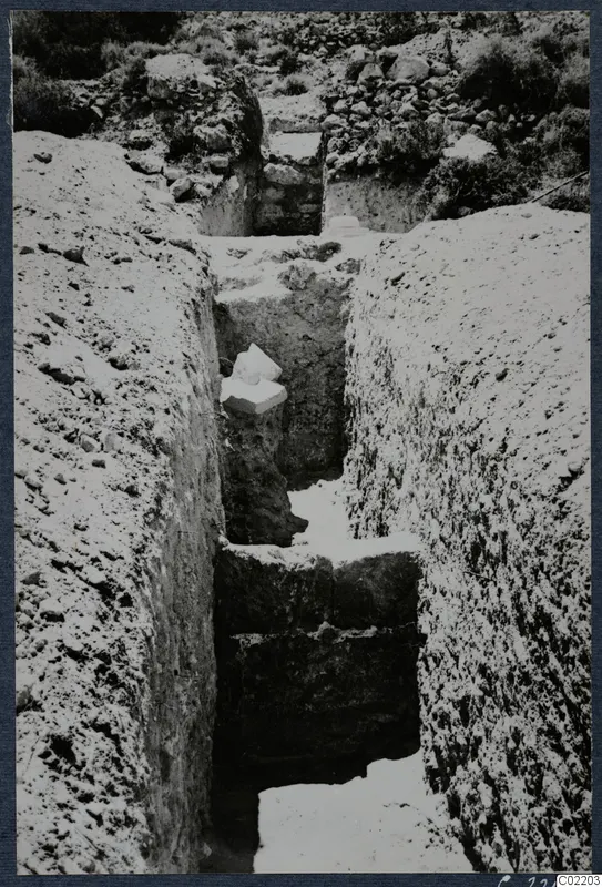 Narrow excavation trench at Vouni Palace with pale stones and objects lying on ledges in the cut
