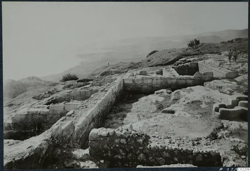 Excavated stone walls at Vouni Palace on a hilltop, with two people walking along the ridge at upper right