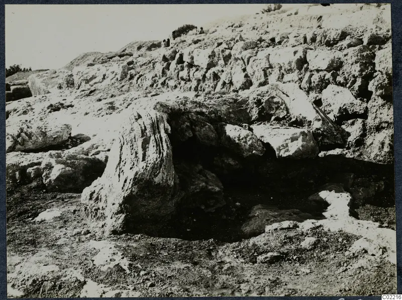 Large rock blocks and a rough stone wall on a slope at Vouni Palace, with small figures on the hillside above.
