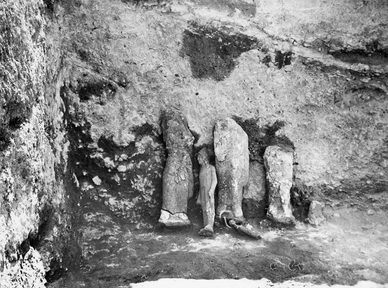 Stone statues standing against the rock-cut back wall of room 117 at Vouni, finds in situ.