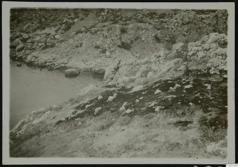 Rocky coastline with water on the left at Petra tou Limniti, with rough stony slopes rising behind.