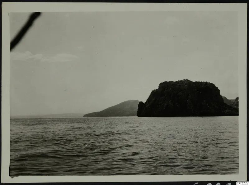 Dark rocky headland rising from the sea at Petra tou Limniti under a pale sky.