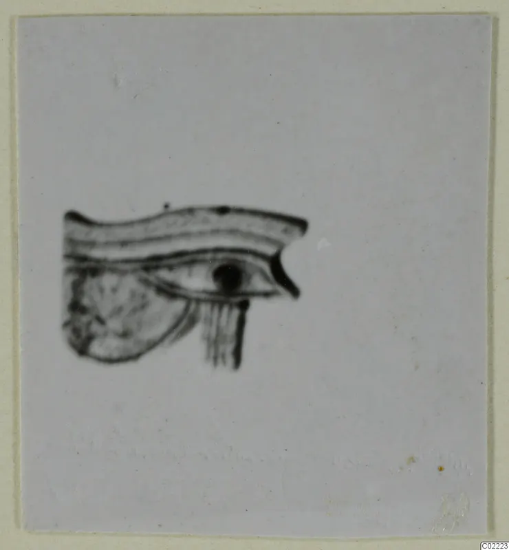 Blurred photograph of a small stylised eye-shaped motif with a curved brow band, mounted on a pale card.