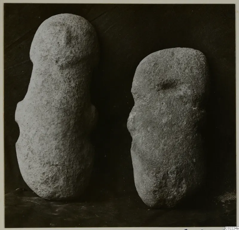 Two roughly shaped stone objects standing upright against a dark background, from Petra tou Limniti.