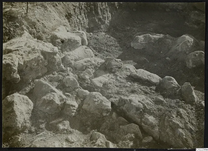 Excavation at Ayios Iakovos with many large pale stones and blocks lying in loose soil.