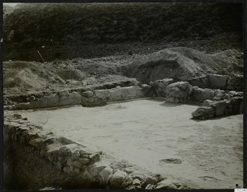 Excavated area at Ayios Iakovos with low stone walls around a pale floor surface.
