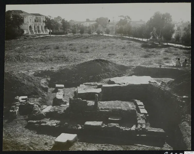 Excavated stone walls and foundations at the eastern part of Bamboula, with a building in the background