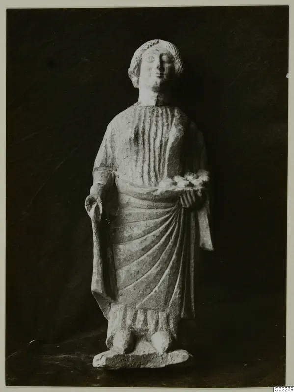 Limestone statuette from Vouni of a standing figure in a draped garment, holding a small dish at chest height.