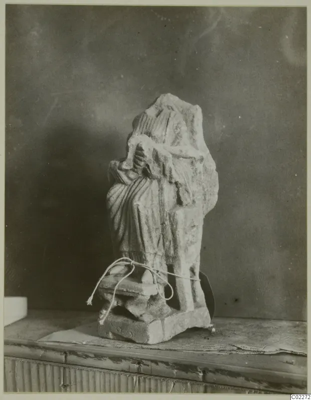 Limestone statue of a draped standing figure with its head and upper part broken away, on a square base