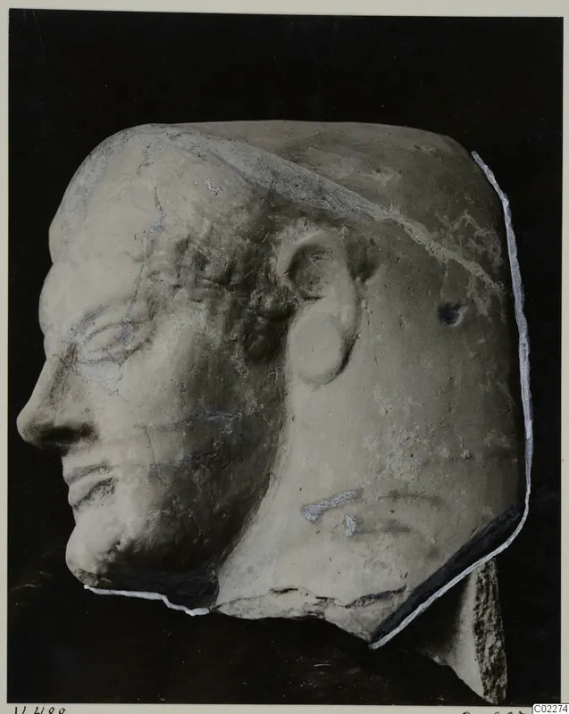 Head of a sculpted figure in left-facing profile, in a pale material, on a dark background