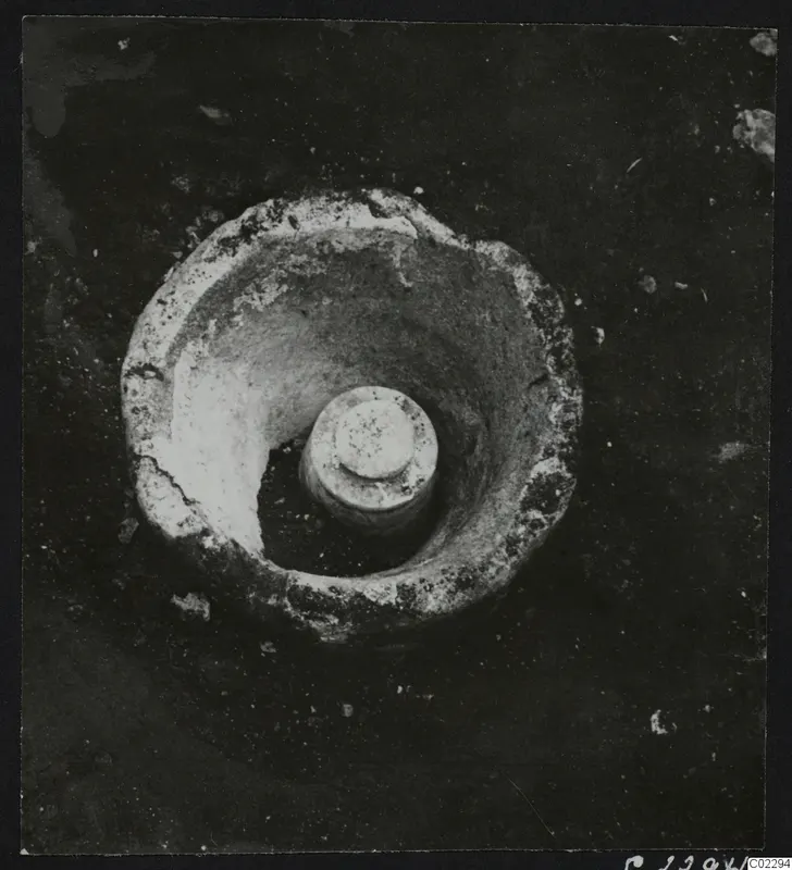 Round pale object with a raised central cylinder, seen from above in excavated soil at Amathus