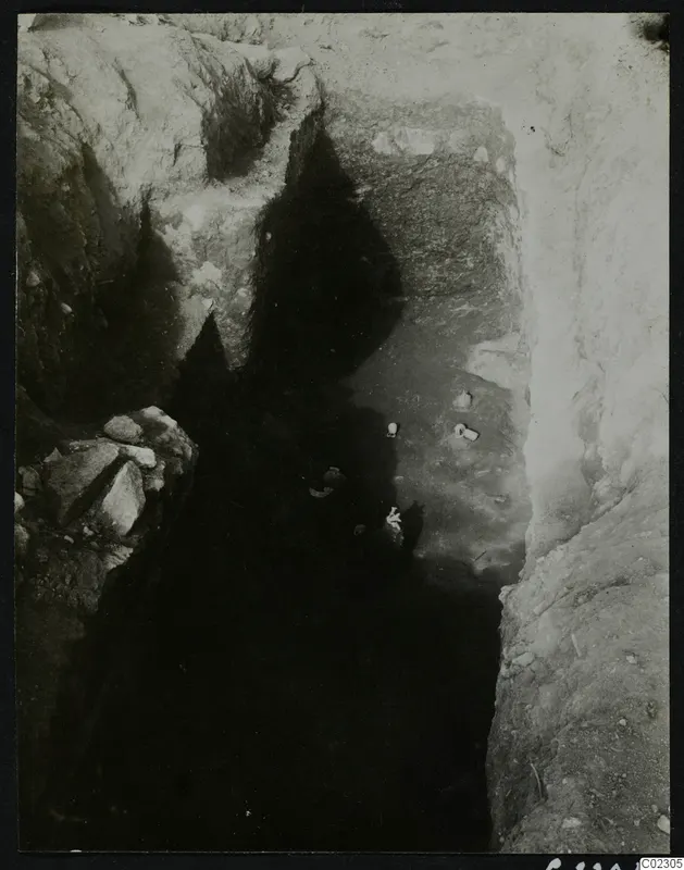 Deep excavation cutting at Amathus with pale objects on the floor and loose stones at one side