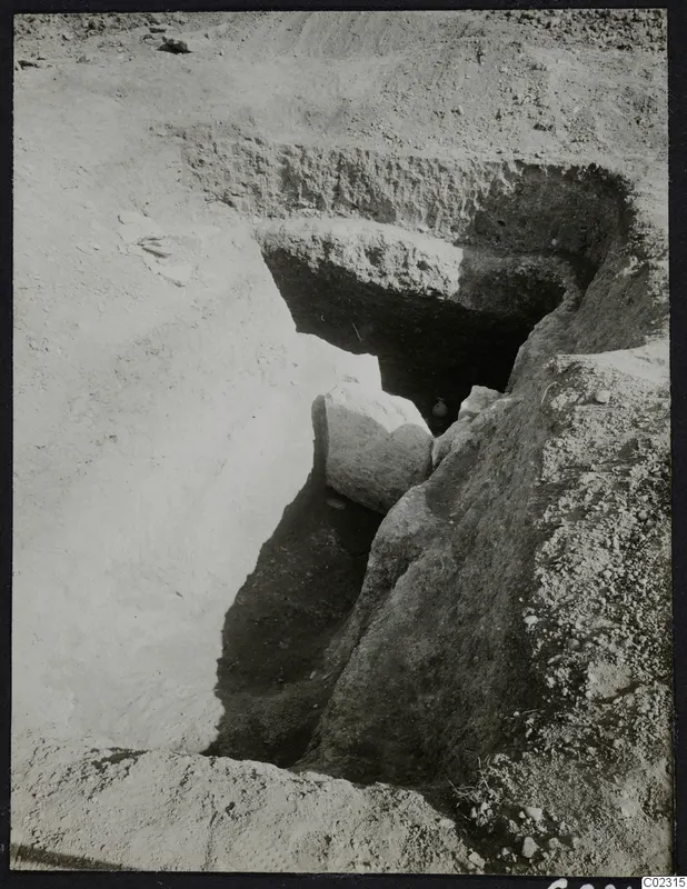Excavation at Amathus: a sloping cut in pale soil leads to a dark opening, with a large fallen stone block in front of it