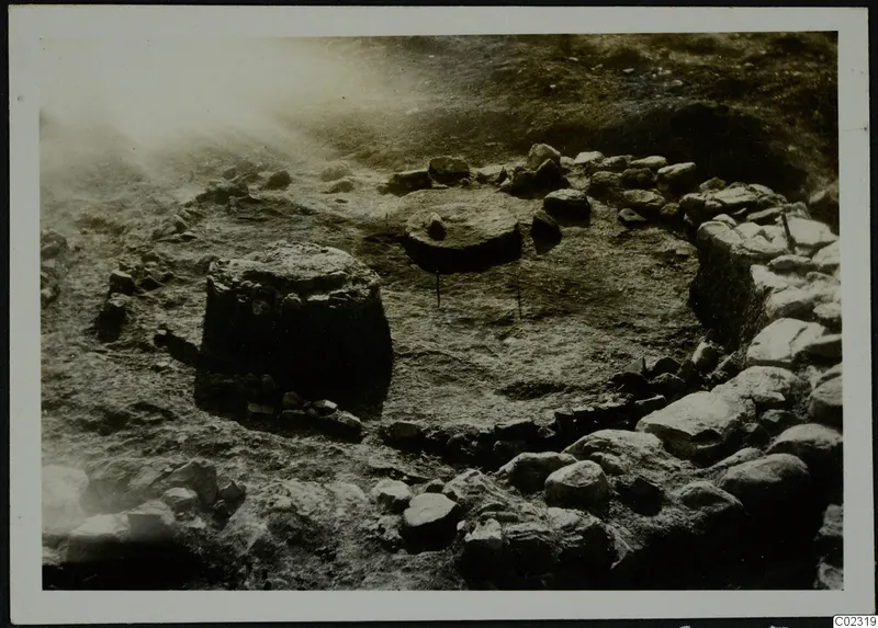 Excavated circular stone construction at Kythrea, with a flat round stone slab at the centre and a stone block at the left.