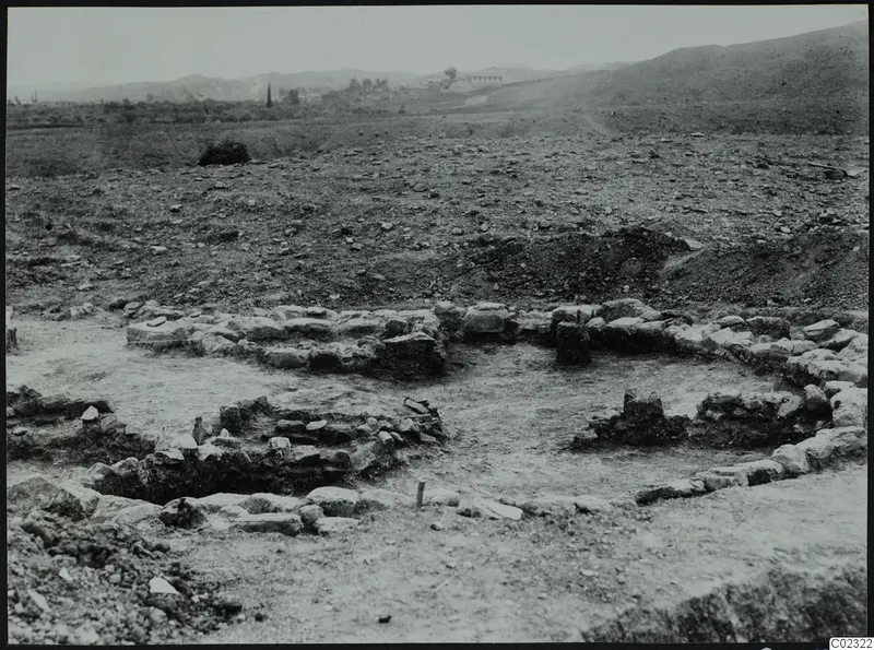 Excavated stone wall foundations at Kythrea, with a rocky hillside and hills behind.