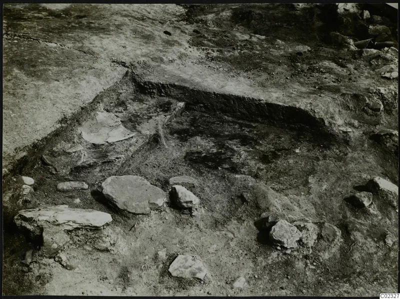 Excavation trench at Kythrea with scattered stones and a pale curved fragment on the trench floor