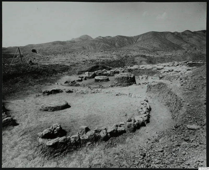 Excavated house foundations with low stone walls and round stone bases on a bare floor, with hills behind, at Kythrea