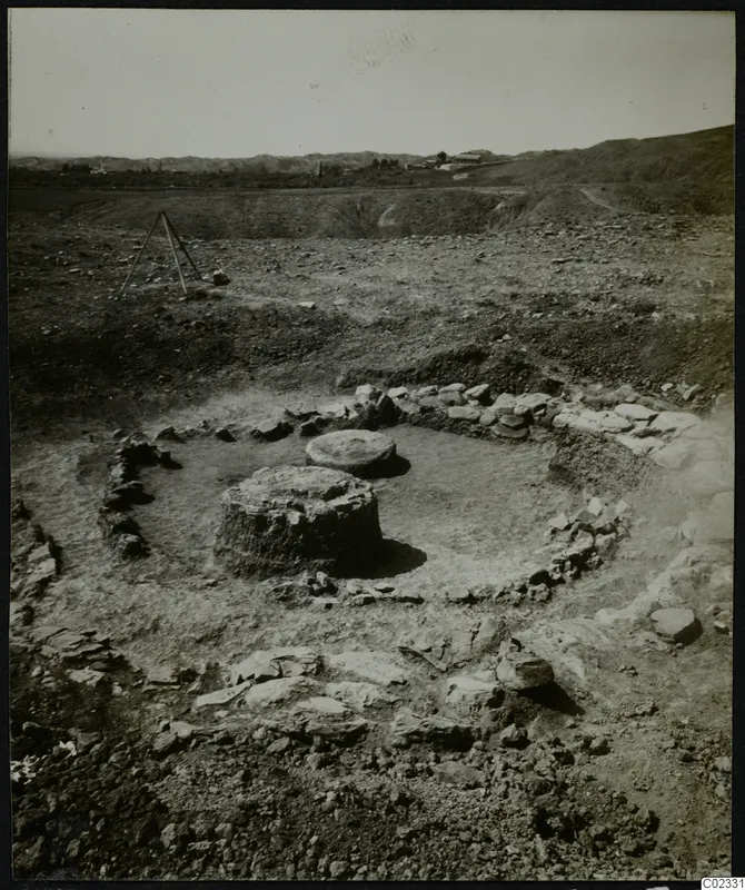 Excavated circular stone foundations at Kythrea, with two rounded stone blocks inside and hills behind.