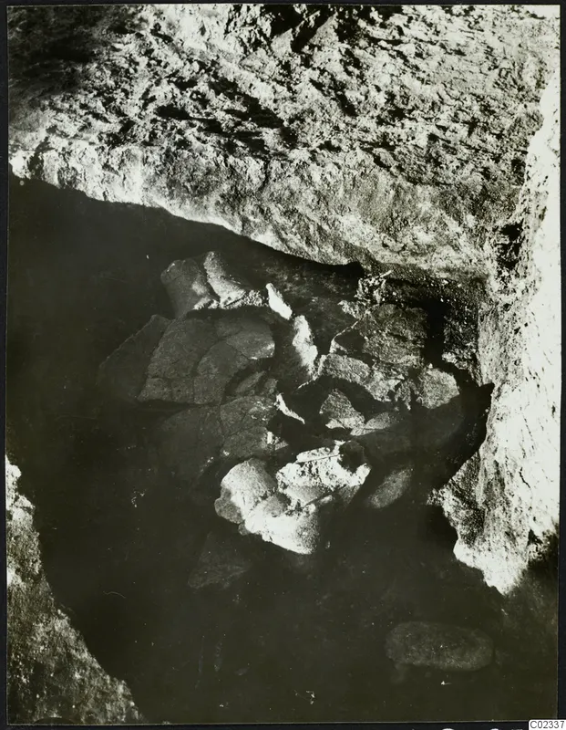 Excavation at Kythrea showing broken objects lying in a rock-cut hollow beneath an overhanging rock face.