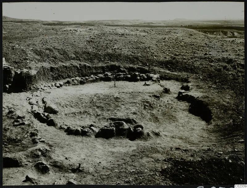 Excavated stone foundations of a round structure in open dry ground at Kythrea