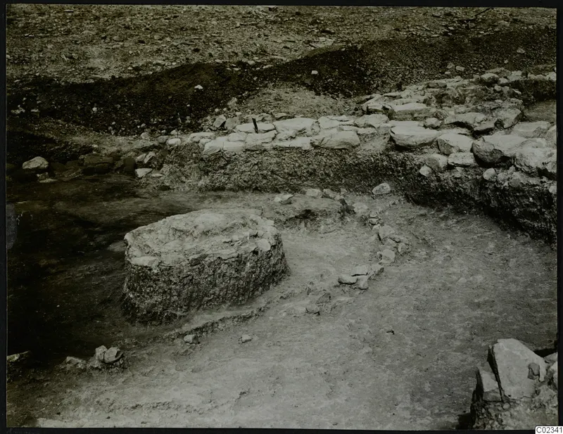 Excavation at Kythrea showing a stone wall and a round stone base in an excavated area