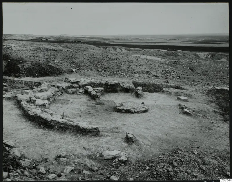 Excavation at Kythrea showing a curved stone wall around a low circular stone base on bare excavated ground
