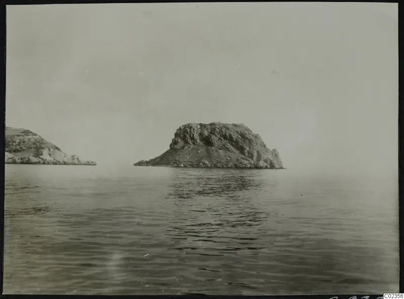 Rocky islet rising from calm sea at Petra tou Limniti, with a second rocky headland at left.