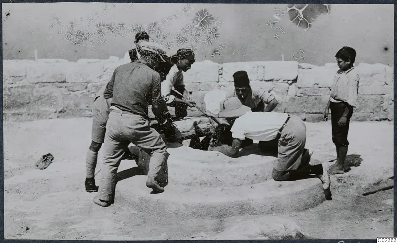 Men and a boy working around a round stone block with a wall of large stone blocks behind them, at Vouni.