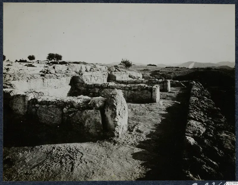 Excavated stone walls and foundations of the palace at Vouni, with a stone-lined passage and open hills behind.