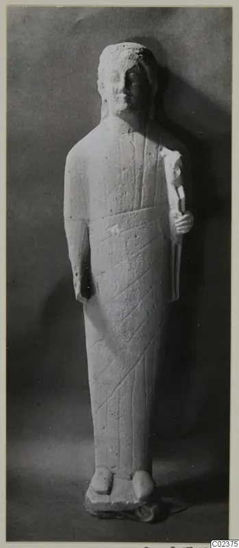 Limestone statue of a standing figure in a long garment, one hand holding an object at the chest, head and feet partly worn.