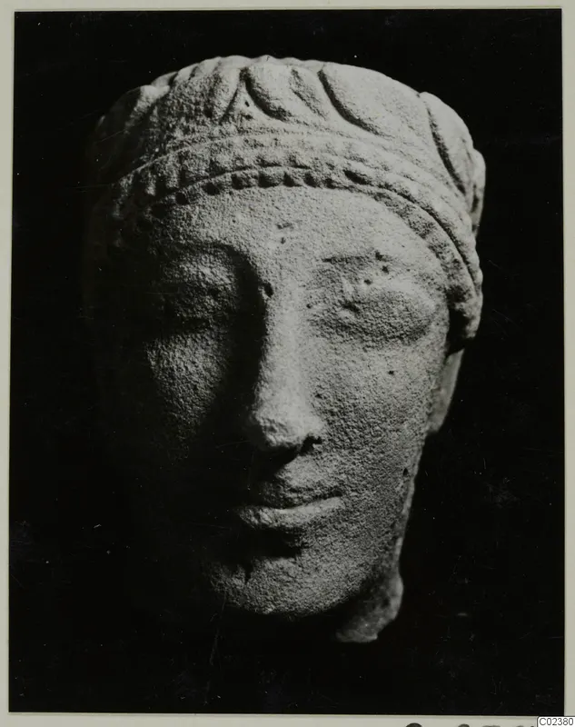 Limestone head from Kition with a carved headband and leaf pattern, photographed against a dark background.