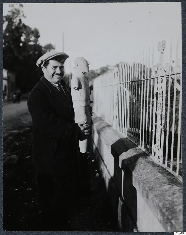 Toulis Souidos smiling and holding a male terracotta sculpture from Ayia Irini beside an iron railing fence