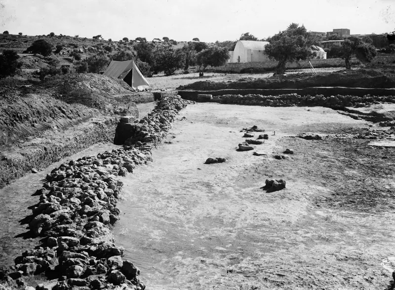 Excavated area at Ayia Irini with a long stone wall on the left, a tent and a white building behind.