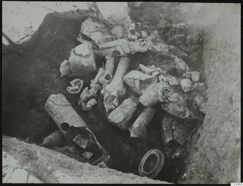 Broken pale ceramic objects lying in situ in an excavated trench at Ayia Irini
