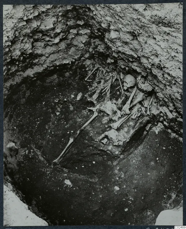 Skeleton lying in an excavated pit at Enkomi, with a skull and long leg bones visible and stones scattered on the floor
