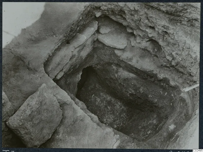Tomb 7 at Enkomi during excavation, showing the tomb chamber cut into soil with large stones.