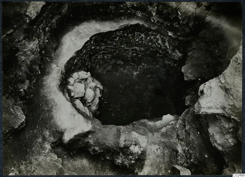 Excavation at Enkomi, looking down into a round cut in rock with a cluster of stones against its rim
