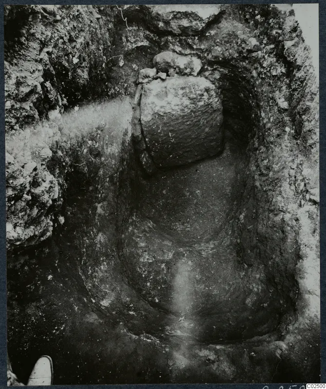 Enkomi excavation: a cut in the ground with large stones at the top and a shoe at the lower left edge.
