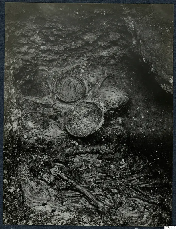 Tomb 14 at Enkomi during excavation, with round vessels and skeletal remains in dark soil