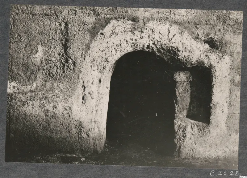 Built tomb chamber seen through a plastered arched doorway, with a recess beside it holding an upright object