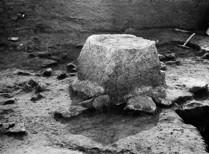 Altar in Late Archaic condition at Ayia Irini, a large rounded stone block with a hollow top in an excavation trench.