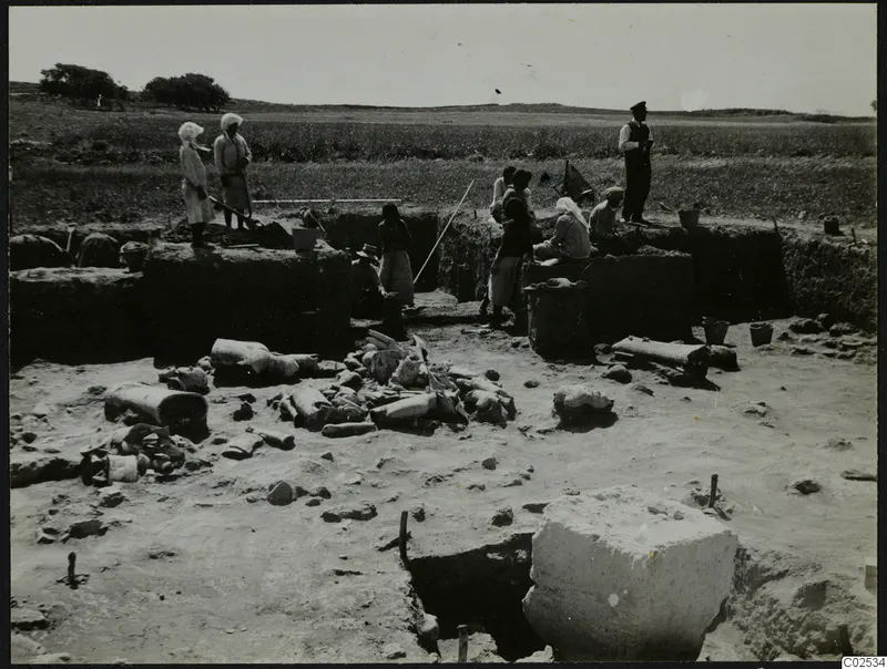 In situ broken pottery in an excavation trench at Ayia Irini, with workers standing and sitting along the trench edges.