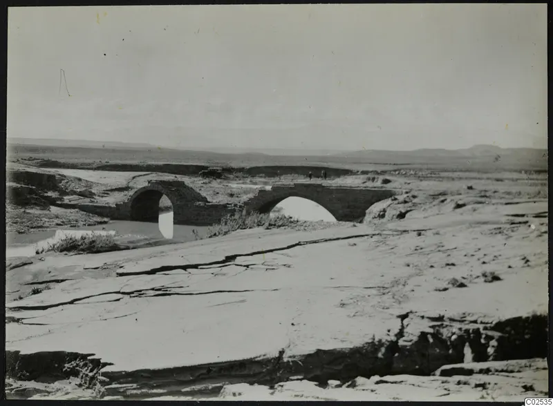 Stone arched bridge over a stream at Ayia Irini, with two small figures on the far bank