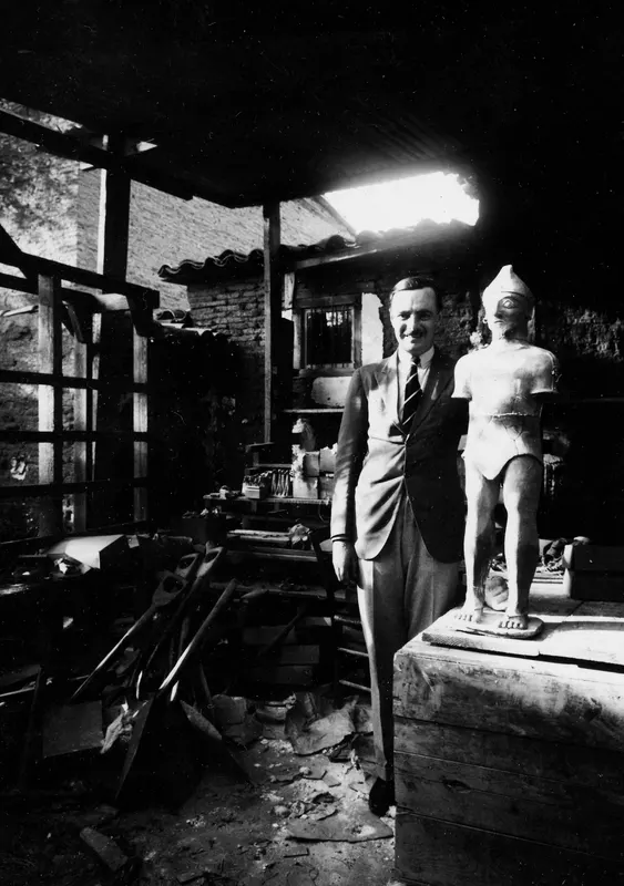 Rubert Gunnis standing beside a large sculpture of a standing figure in a storeroom at Nicosia.