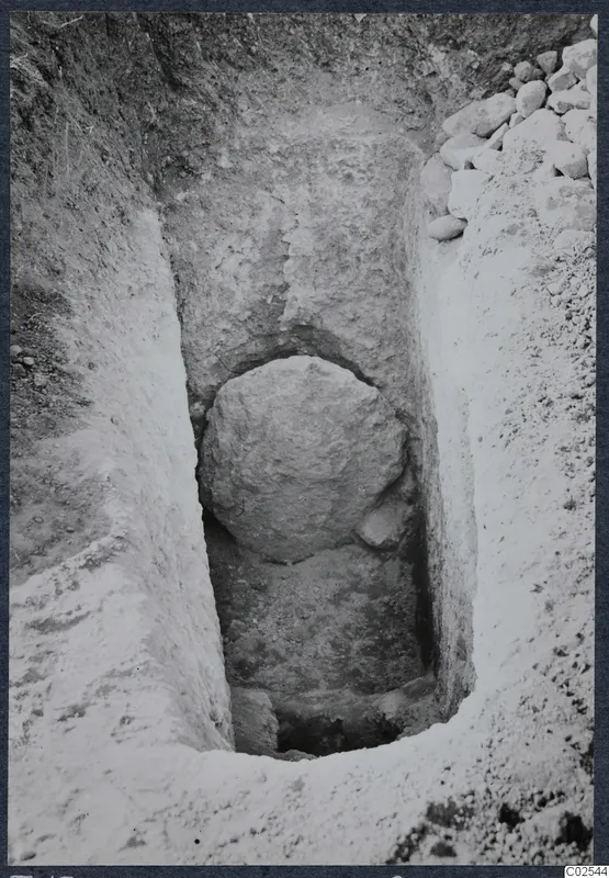 Excavation trench at Ayios Iakovos with a large rounded stone set against the cut face and a heap of stones at the edge